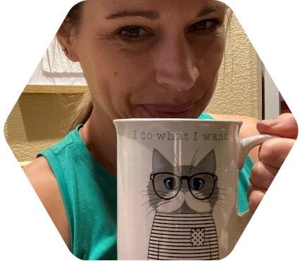 Kristen holding a coffee cup that has a cat with a striped shirt and glasses and the text above the cat reads I do what I want.